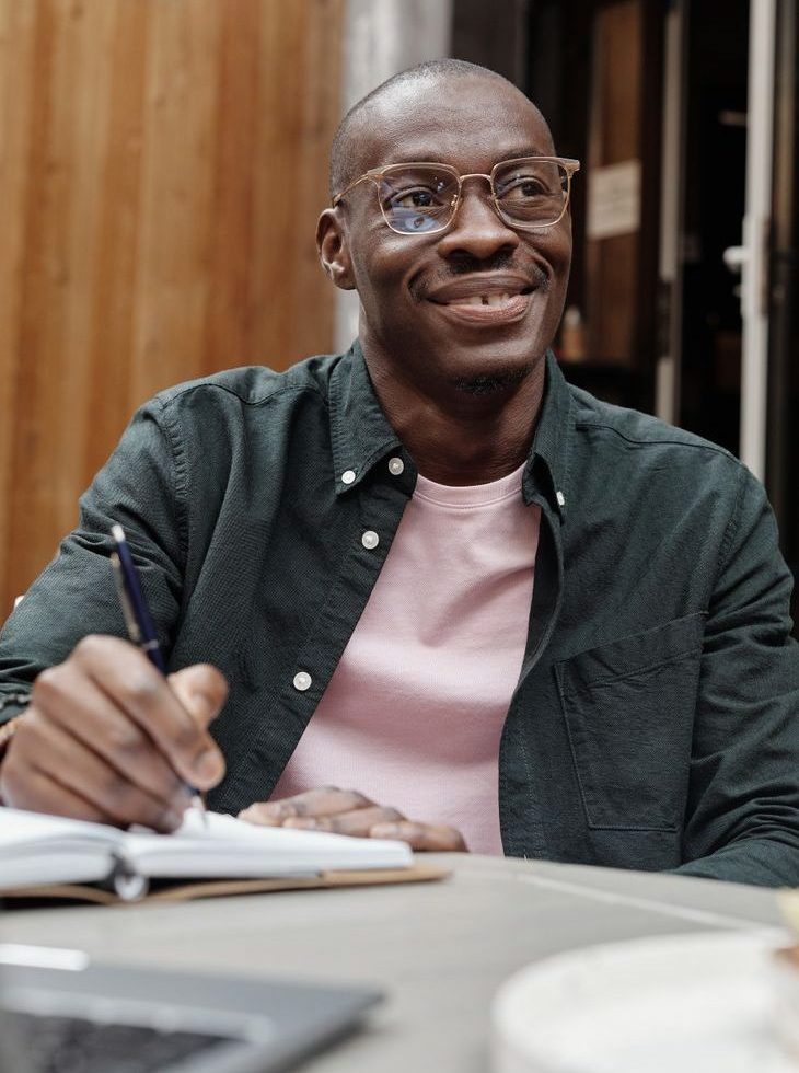 a man wearing eyeglasses holding a pen on a notebook